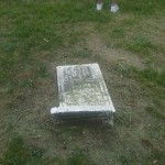 A person stands beside a tombstone in a grassy field, reflecting on the serene surroundings